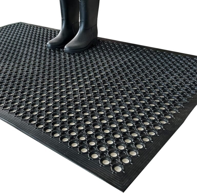 Black Uniboho rubber floor mat with circular drainage holes and person in rubber boots standing on anti-slip surface