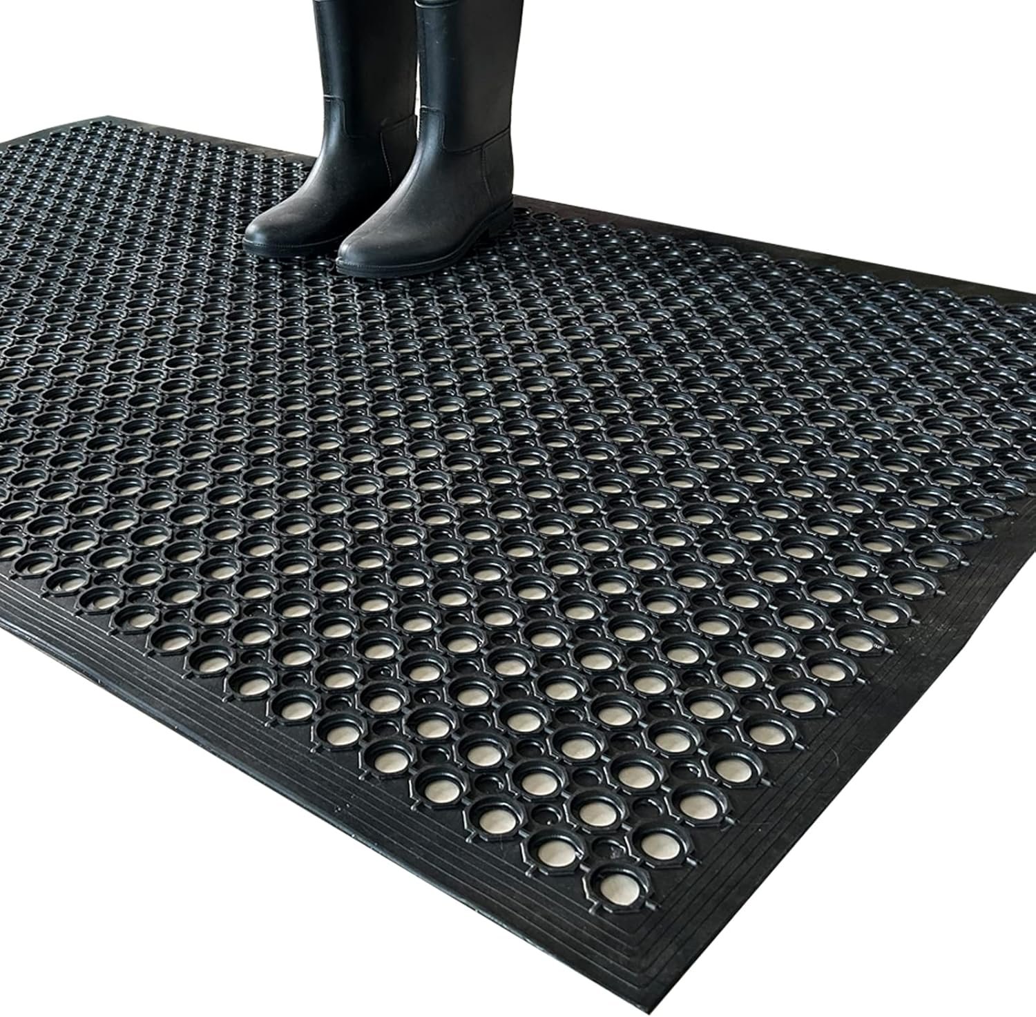 Black Uniboho rubber floor mat with circular drainage holes and person in rubber boots standing on anti-slip surface