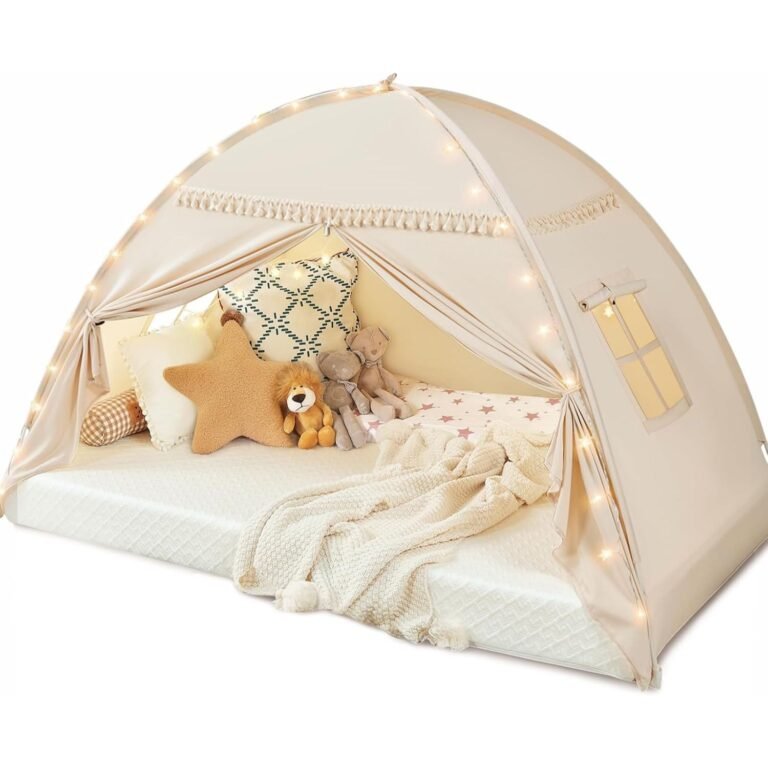 Cream canvas kids bed tent with LED lights and macrame trim containing cozy bedding, pillows, and stuffed animals